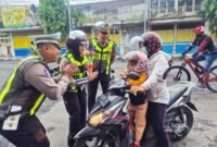 Petugas Satlantas Polres Lumajang saat menyapa pengendara motor tertib berlalu lintas dengan memberikan bunga